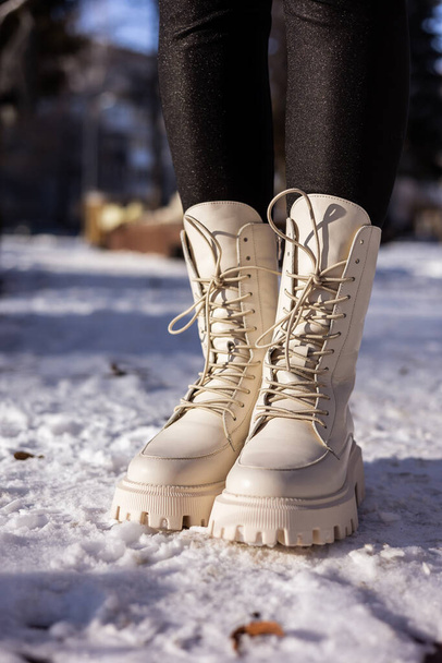 Woman in fashionable white boots on white snow, close-up. Women's legs in stylish winter leather boots - Photo, image