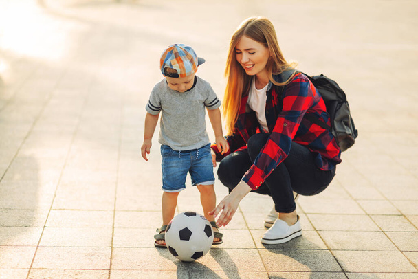 Boldog család focizni nyáron, anya és fia játszani és futni a parkban egy gyönyörű reggel. Egy fiú focizik, miközben a családjával játszik. Családi fogalom - Fotó, kép