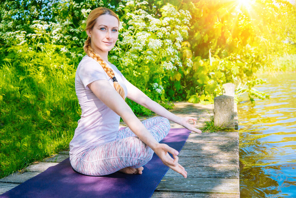 fiatal nő jóga ászana a parkban. lány nyújtás gyakorlat jóga pozícióban. boldog és egészséges nő ül lótuszpozícióban és jógázik. meditáció és sport a szabadban. - Fotó, kép