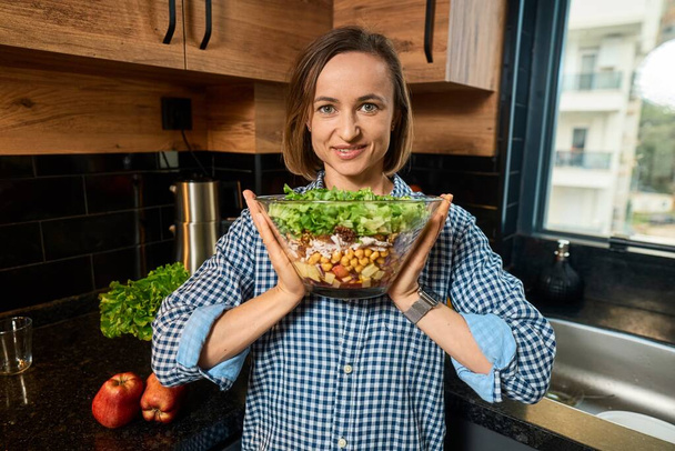 Egészséges étel otthon. Gyönyörű kauázusi nő áll mosolyogva tartó tál saláta egy egészségügyi reggeli boldogsággal a konyhában otthon. Életmód és egészséges koncepció - Fotó, kép