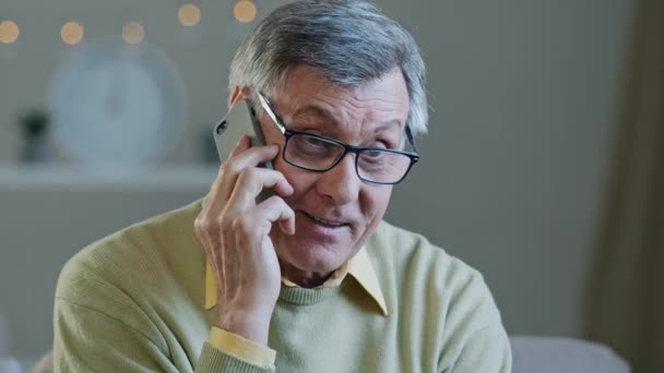 Muotokuva harmaa tukka vanhempi mies lasit puhua puhelimessa hymyilevä vanhusten isoisä chattailuun iloisesti käyttää mobiili jakaminen hyviä uutisia lasten kanssa onnellinen vuotiaiden mies levätä kotona nauttia miellyttävä keskustelu - Materiaali, video