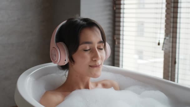 Žena si koupel poslech hudby ve sluchátkách v koupelně - Záběry, video