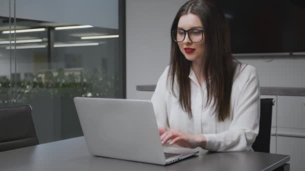 Kancelářská práce. Mladá dáma manažerka ve formálním oblečení a brýlích pracuje na notebooku a usmívá se, stopa výstřel, volný prostor - Záběry, video