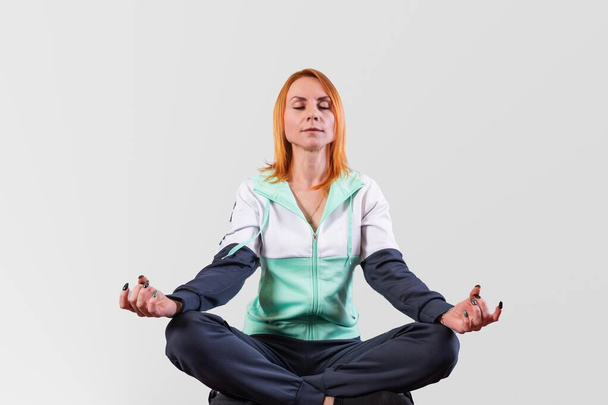 Das Mädchen im Trainingsanzug sitzt in der Lotusposition auf grauem Hintergrund. Hochwertiges Foto - Foto, Bild