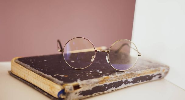 The glasses are on an old and shabby book, on a bookshelf in the library. Concept: reading books - Foto, imagen