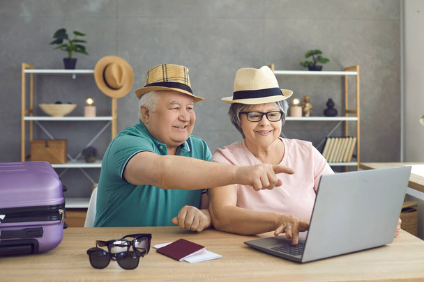 Happy senior couple at home using a laptop to pay for tickets and book a room online. - Foto, imagen