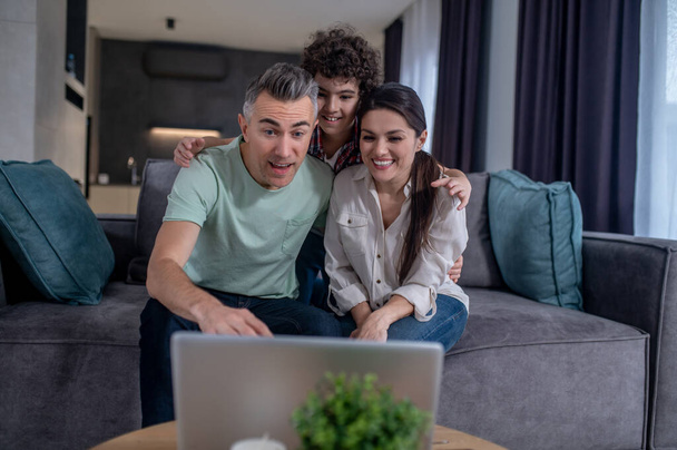 Boy hugging parents looking at laptop sitting on sofa - Foto, immagini