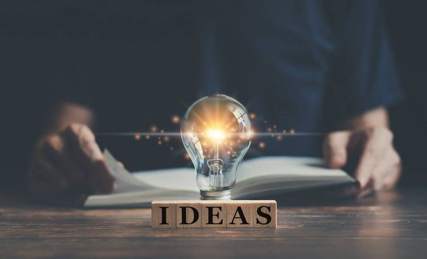 Man or adult learning book or reading textbook and glowing light bulb with IDEAS word. Idea of studying in education or business. Success concept of knowledge or cognition inspiration and motivation - Photo, Image