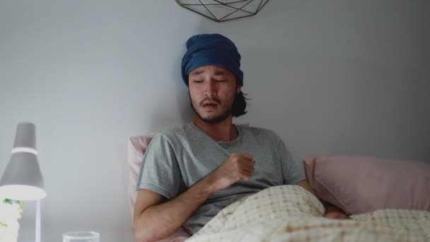Ázsiai férfi köhög és iszik vizet, míg otthon a hálószobában. Fiatal férfi egészségügyi és egészségügyi ellátás. - Felvétel, videó