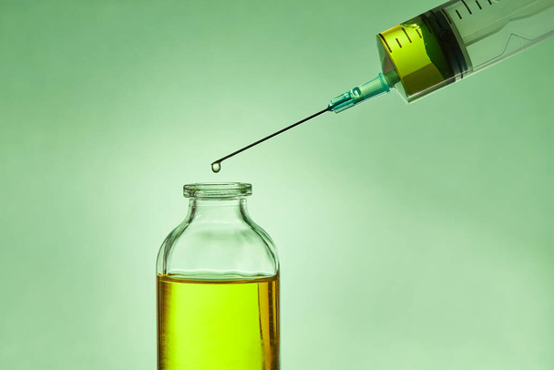 A drop of liquid drips from the needle of a medical syringe into the bottle. - 写真・画像