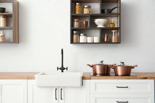 Интерьер светлой кухни со столешницами, кастрюлями и раковиной - Фото, изображение