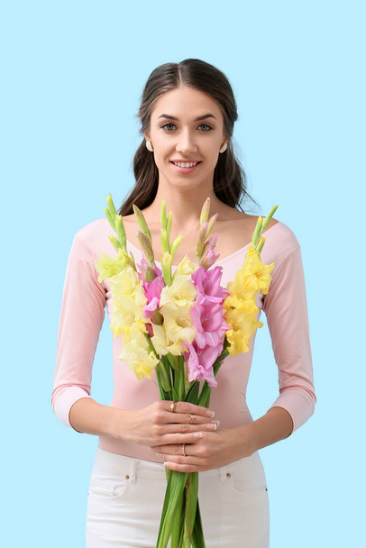 Joven mujer sonriente sosteniendo ramo de flores de gladiolo sobre fondo de color - Foto, imagen