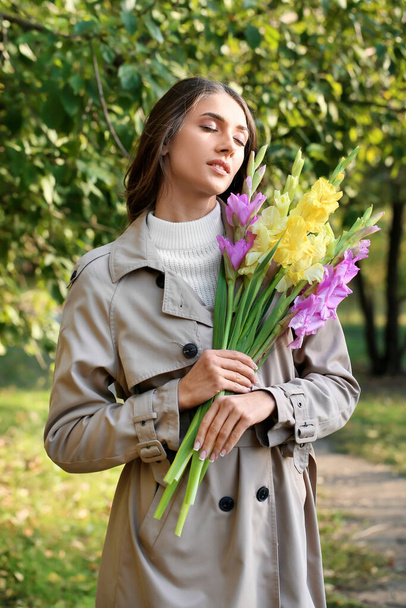 Jovem mulher com olhos fechados segurando buquê de flores Gladiolus no parque - Foto, Imagem