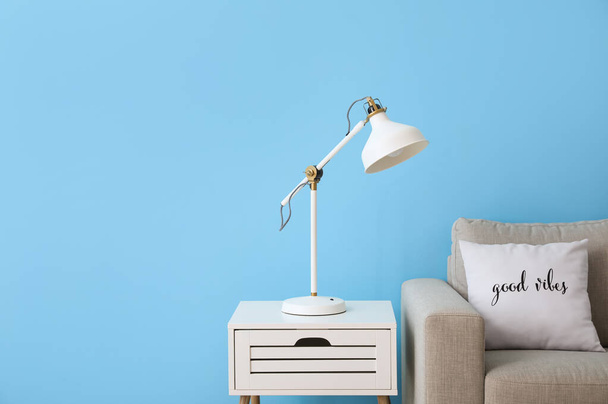 Stół z białą lampą i kanapą w pobliżu niebieskiej ściany - Zdjęcie, obraz