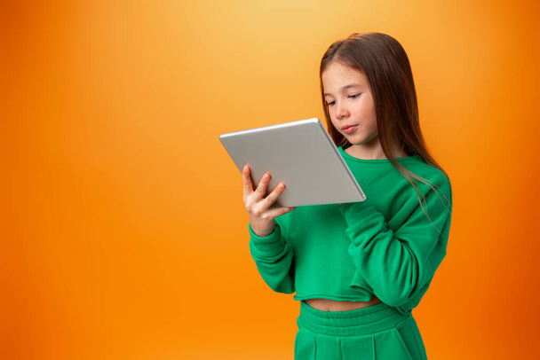 Beautiful teen girl using digital tablet over orange studio background - Foto, Bild