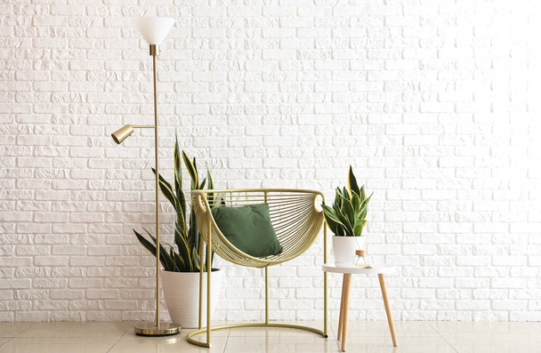 Lampe debout dorée, fauteuil et plantes d'intérieur près du mur de briques blanches - Photo, image