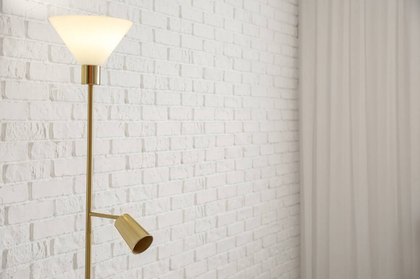 Beyaz tuğla duvarın yanında parlayan standart lamba, yakın plan. - Fotoğraf, Görsel