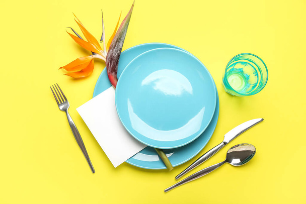 Eenvoudige tafelschikking met paradijsvogel bloem en blanco kaart op gele achtergrond - Foto, afbeelding