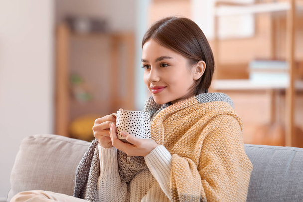 Beautiful young woman drinking tasty tea on sofa at home - Фото, зображення