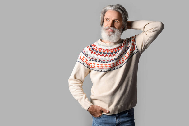 Knappe oudere man in gebreide trui op grijze achtergrond - Foto, afbeelding