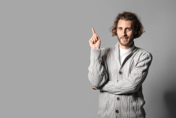 Hezký mladý muž v pleteném svetru ukazuje na něco na šedém pozadí - Fotografie, Obrázek