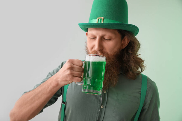 Hombre barbudo bebiendo cerveza sobre fondo claro. Celebración del Día de San Patricio - Foto, imagen