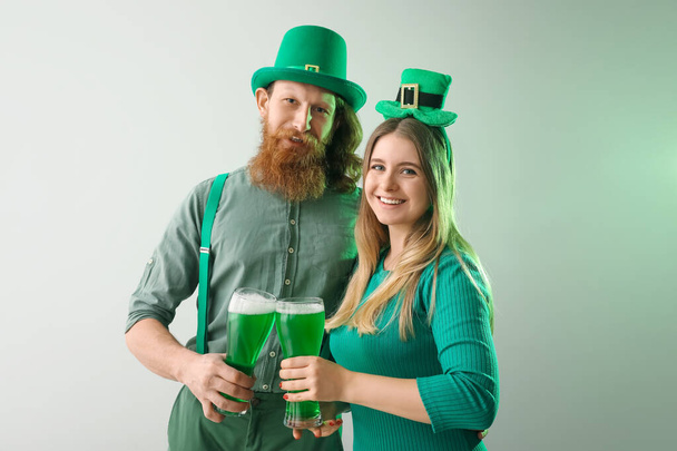 Jovem casal feliz com copos de cerveja no fundo claro. Celebração do Dia de São Patrício - Foto, Imagem