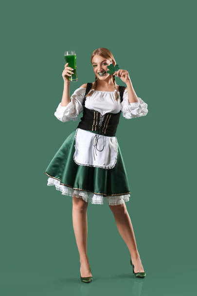 Piękna irlandzka kelnerka ze szklanką piwa i koniczyną na zielonym tle. Święto św. Patryka - Zdjęcie, obraz