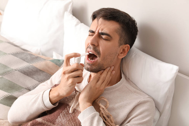 Młody człowiek z bólem gardła przy użyciu inhalatora w łóżku - Zdjęcie, obraz