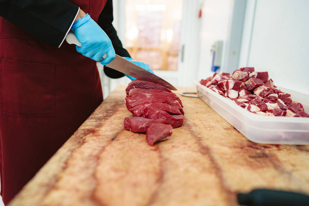 Butcher cutting slices of raw meat on wooden board - Фото, зображення