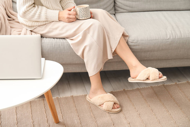 Mujer joven en suaves zapatillas cómodas bebiendo té en casa - Foto, Imagen