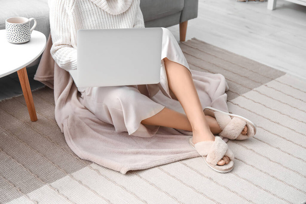 Giovane donna in morbide comode pantofole utilizzando il computer portatile a casa - Foto, immagini