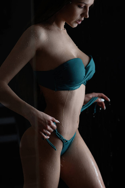 Szexi karcsú barna, hosszú nedves haj visel kék fürdőruha, csupasz vállak és hasérintő test, miközben néz le a fekete háttér - Fotó, kép