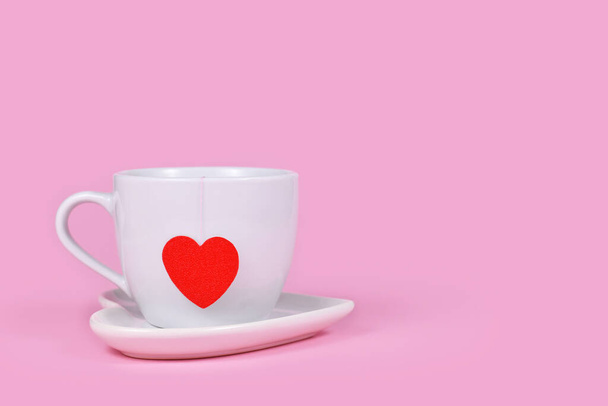 Tea cup with red heart shaped tea bag paper on pink background with copy space - Foto, Imagen