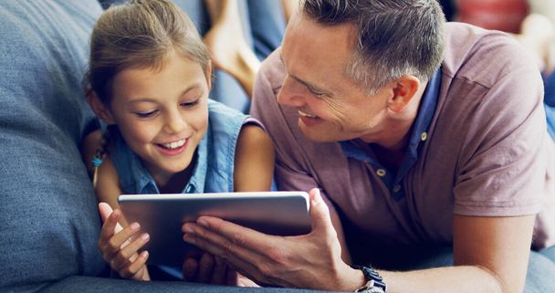Lessons from dad in online safety. Shot of a cute little girl using a digital tablet with her father on the sofa at home. - Foto, imagen
