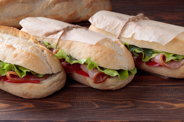 Крупный план трех сэндвичей "бан ми" с нарезанной свининой и перцем и салатом, упакованными в бумагу на деревянном фоне. Мягкий фокус. - Фото, изображение