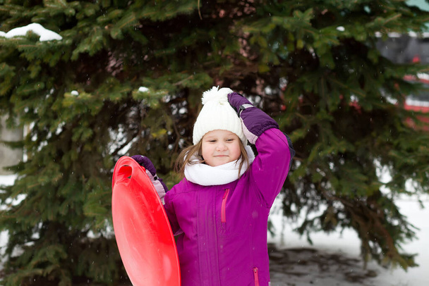Diversión familiar, actividad de invierno para niños en manoplas nevadas. Chica sonriente con estilo en sombrero blanco, abrigo, bufanda, snood.Happy niños de moda que ponen en la nieve. Juegos al aire libre, caminar en un hermoso bosque, parque, árboles. - Foto, imagen