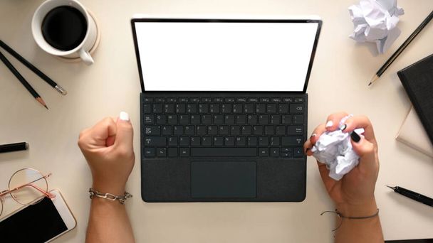 女性従業員は彼女の仕事の報告書に不満を持っています,彼女の手とオフィステーブルの上に紙の砕いた部分を持つタブレットコンピュータに取り組んで.トップビュー - 写真・画像
