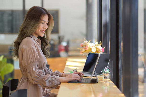 Сторона зору, прекрасна азіатська бізнесменка працює на планшеті Touchpad, набираючи на бездротовій клавіатурі за кафе стіл. - Фото, зображення