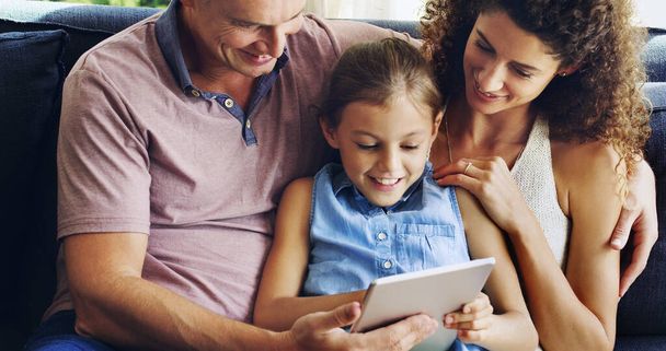 El tiempo en familia se ha vuelto aún más divertido. Foto de una linda niña usando una tableta digital con su madre y su padre en el sofá en casa. - Foto, Imagen