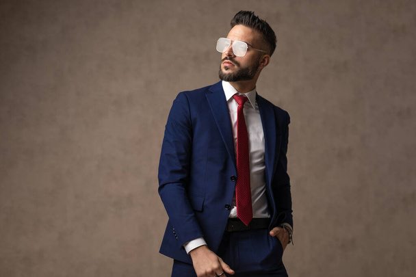 attractive businessman wearing eyeglasses, holding one hand in pocket and looking away  - Foto, immagini