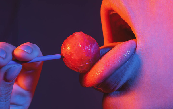 Licking candy. Lollipop model. Woman lips sucking a candy. Glamor sexy model with red lips eat sweats lolly pop on neon lights. - Photo, image