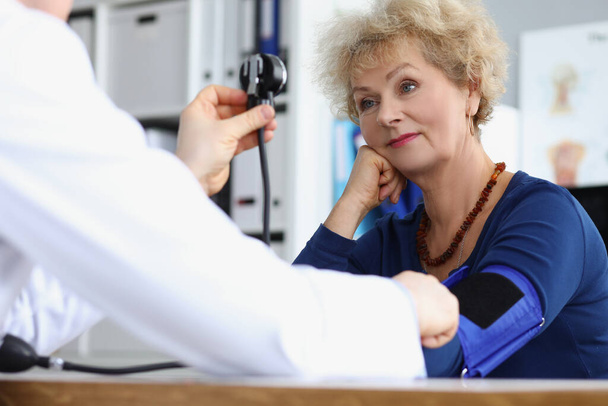 Senior female on appointment, doctor measure blood pressure with equipment - Foto, imagen