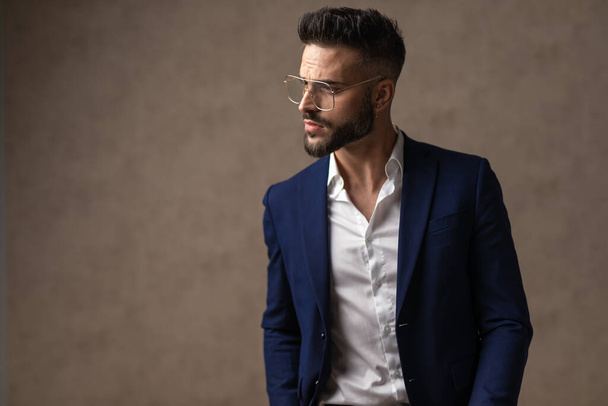 attractive businessman being serious, looking to the side, wearing eyeglasses against wallpaper - Photo, Image