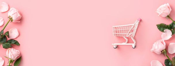 Valentine's Day shopping design concept background with pink rose flower and cart on pink table background - Foto, Imagem