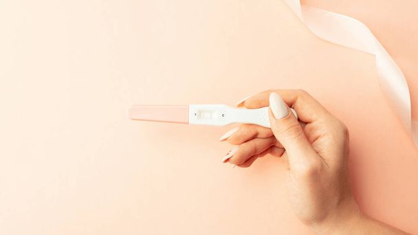 Pregnancy test positive. Female hand hold positive pregnant test with silk ribbon on pink background. Medical healthcare gynecological, pregnancy fertility maternity people concept - Foto, Imagen