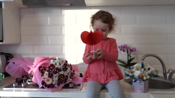 Szczęśliwych Walentynek Słodkie dziecko dziewczyna gra z wystrojem i siedzi na stole w kuchni z kwiatami w domu - Materiał filmowy, wideo