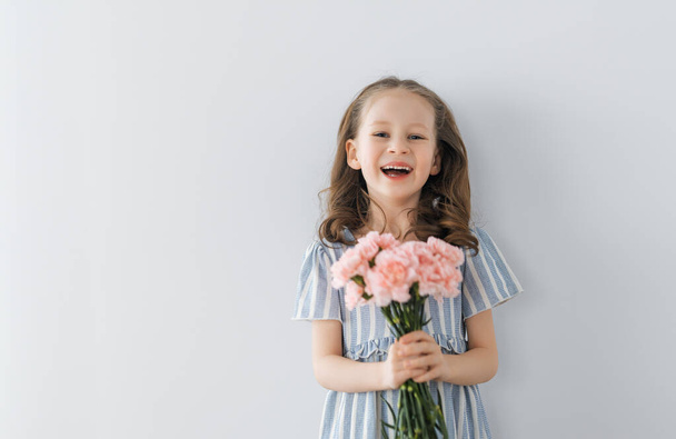 Beautiful girl with pink flowers in hands on grey wall background. - Φωτογραφία, εικόνα