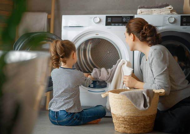 Beautiful young woman and child girl little helper are having fun and smiling while doing laundry at home. - Foto, Imagem