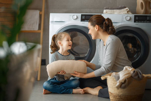Beautiful young woman and child girl little helper are having fun and smiling while doing laundry at home. - 写真・画像